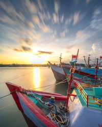 Fishing boats moored at sea against sky during sunset