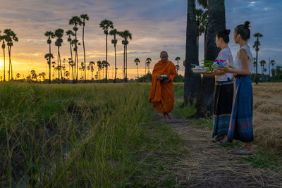 People standing on field against sky during sunset