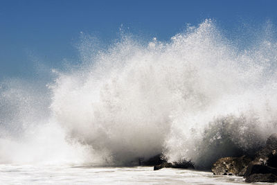 Waves splashing in sea against clear sky during sunny day