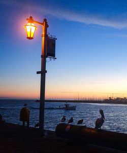 Silhouette people sitting on shore against sky during sunset