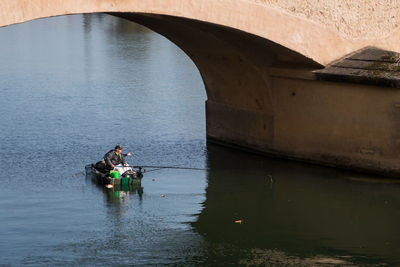 Man fishing while sitting in boat on canal