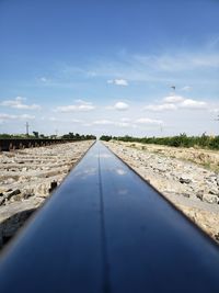 Surface level of railroad track amidst field against sky