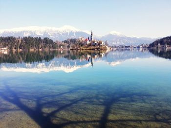 Houses amidst snowcapped mountains reflecting on lake against clear sky