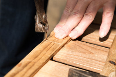 Close-up of person removing rusty nail from wood