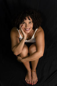 Top view of woman sitting on floor under black cloth smiling with hand on face. 