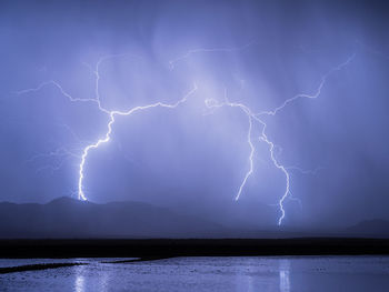 Lightning striking the mountains behind a pond near willcox, arizona