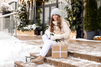 A happy girl in mittens sits on the steps and enjoys gifts on the street in winter