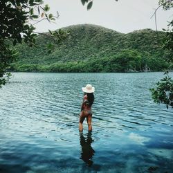 Rear view of young woman standing in lake against sky
