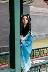 Portrait of young woman standing against railing