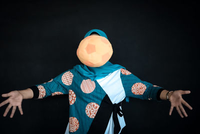 Football hitting on face of woman while standing against black background