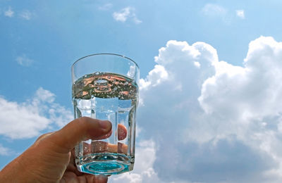 Person holding glass of drink against sky