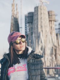 Portrait of young woman wearing sunglasses standing against city