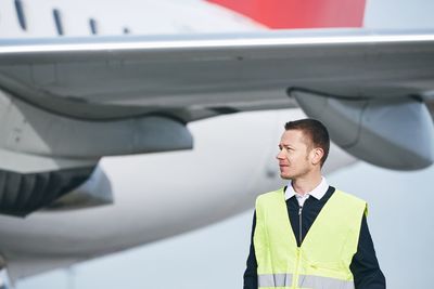 Young man looking away while standing against airplane