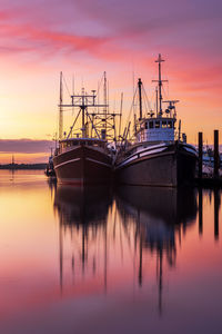 Boats moored in harbor at sunset