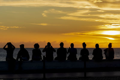Silhouette people standing by sea against orange sky