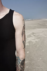 Cropped image of man standing on shore at beach against clear sky