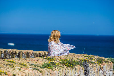 Rear view of woman standing by sea against clear blue sky