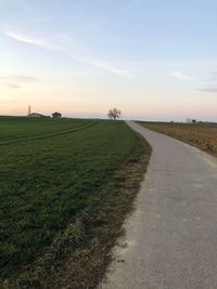 Road amidst field against sky during sunset