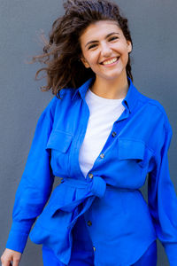 Portrait of young happy woman in blue costume standing against wall