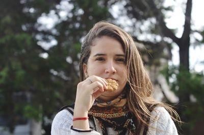 Portrait of young woman having cookie against tree