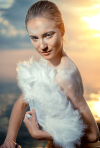 Portrait of female model covering breasts with white feather hand fan at beach