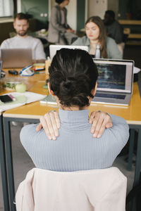 Rear view of exhausted businesswoman rubbing shoulders while working at office