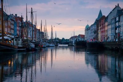 Boats moored in canal by city against sky during sunset