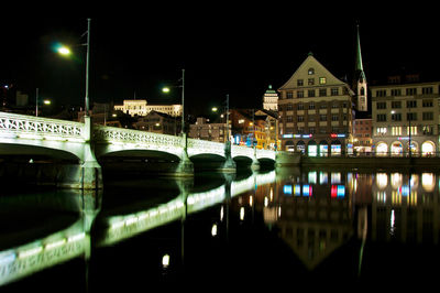 Illuminated buildings by river against sky in city at night