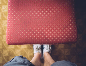 Low section of man standing by red chair at home