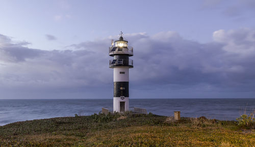 Lighthouse amidst sea and buildings against sky