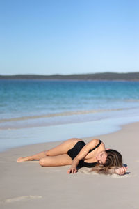 Asleep young woman in black bikini and on beach in eastern australia