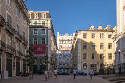 People on street amidst buildings in city against sky