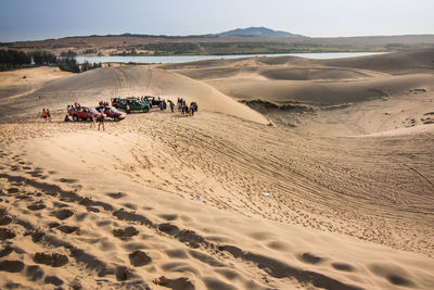 Group of people with vehicles on sand dune in desert