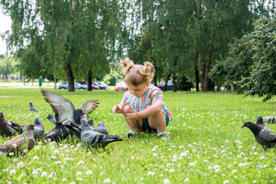 Cute girl crouching on grass with birds