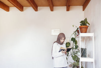 Side view of young woman using mobile phone while standing against wall