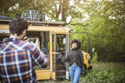 Happy young woman posing against caravan for boyfriend during camping in forest