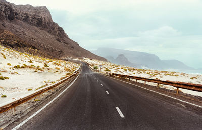 Road leading towards mountains against sky