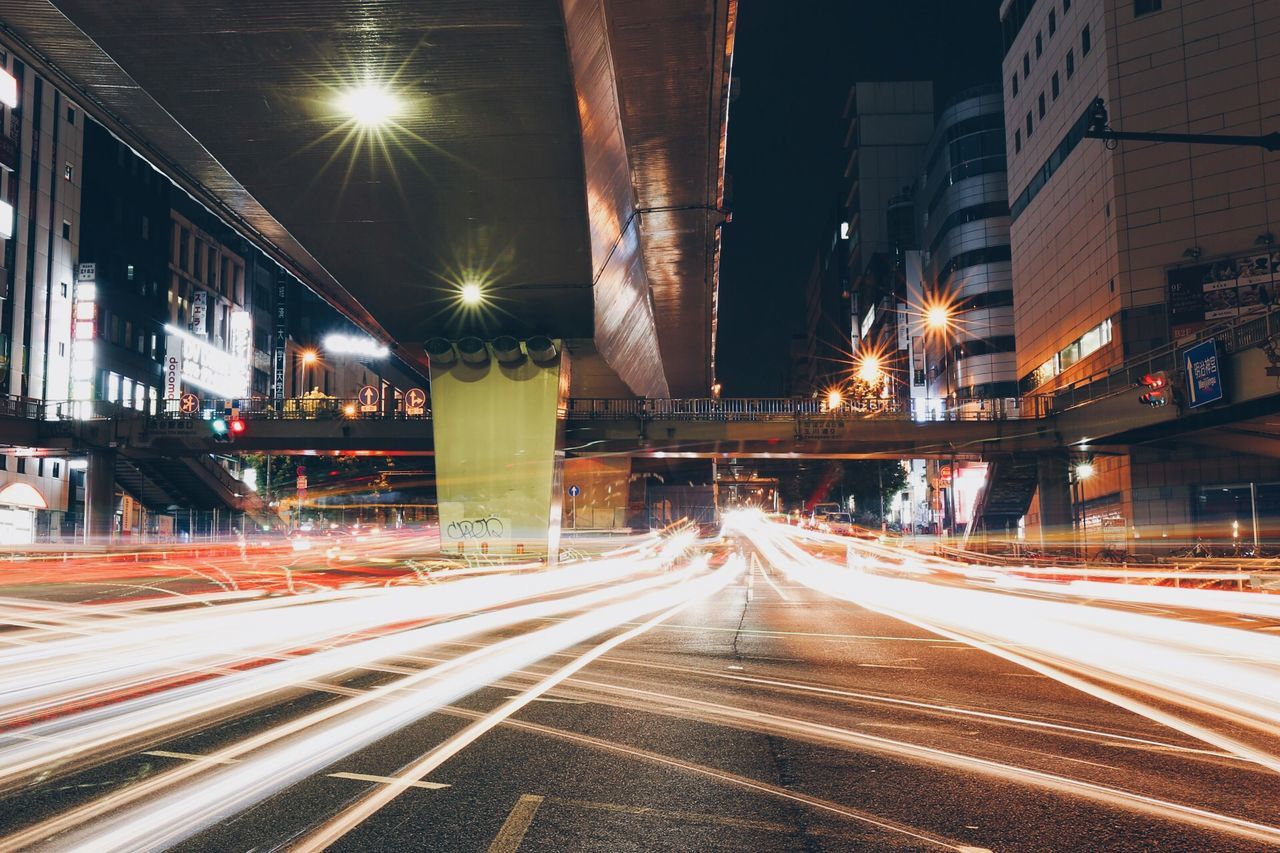 illuminated, transportation, light trail, long exposure, night, speed, built structure, architecture, motion, railroad track, blurred motion, the way forward, city, building exterior, road, railroad station platform, connection, city life, diminishing perspective, travel