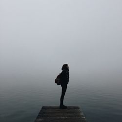 Woman standing on pier over in foggy weather