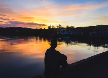 Silhouette man looking at lake against sky during sunset