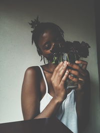 Close-up portrait of woman holding flowers against wall at home