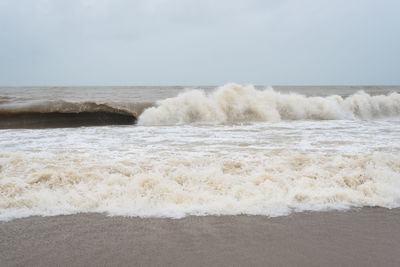 Waves breaking on shore against sky