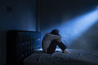 Woman sitting on bed against wall at home