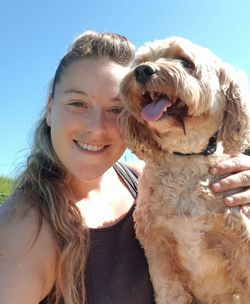 Portrait of smiling mid adult woman with dog standing against clear blue sky during sunny day