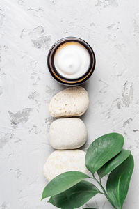 Jar of cosmetic cream with balancing stones on concrete background with green leaves. minimal style