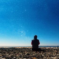 Rear view of man sitting against sea at beach