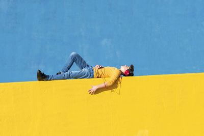 Side view of man sleeping on yellow wall