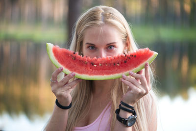 Portrait of young woman holding watermelon slice at lakeshore