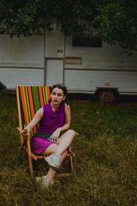 Woman smoking cigarette while sitting on chair over field