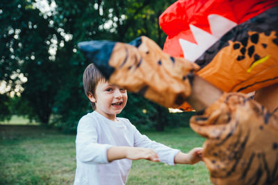 Portrait of cute boy playing with person wearing dinosaur costume in park